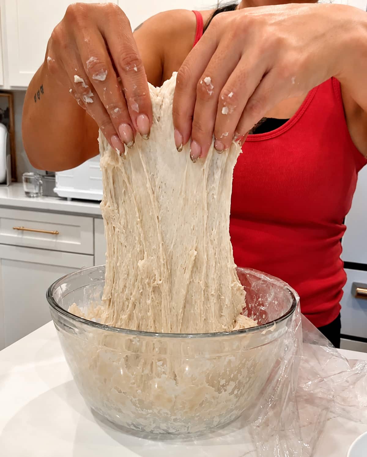 Woman pulling sourdough dough out of a glass bowl.