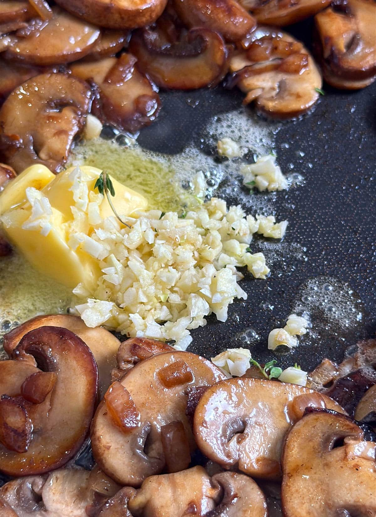 close up of butter and garlic cooking in a pan with mushrooms