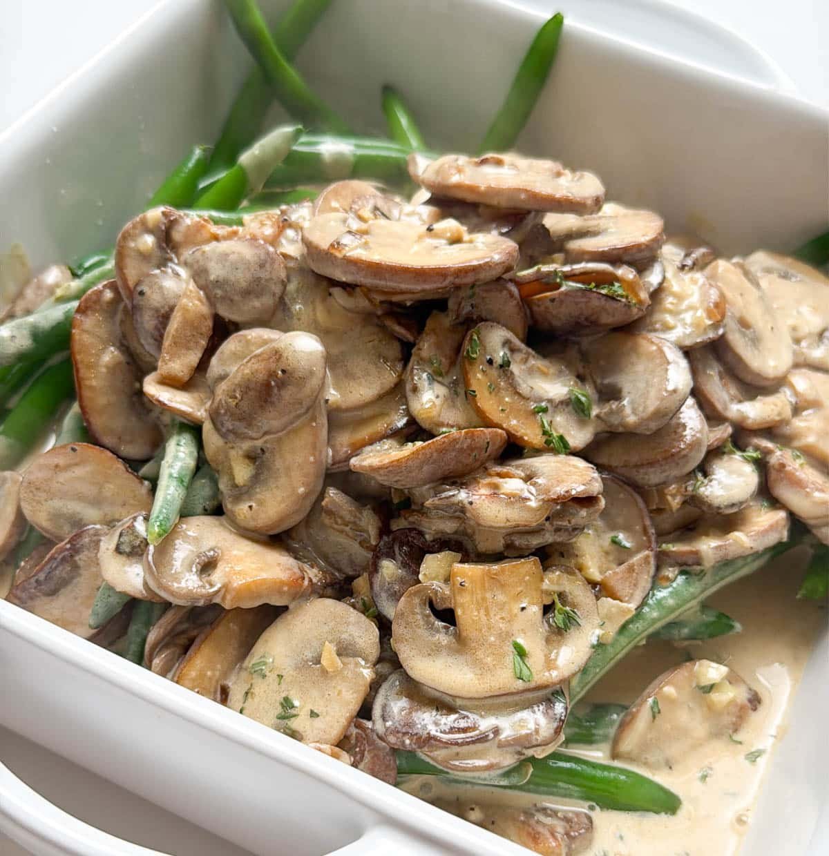 close up of green beans and mushroom sauce in a white casserole dish