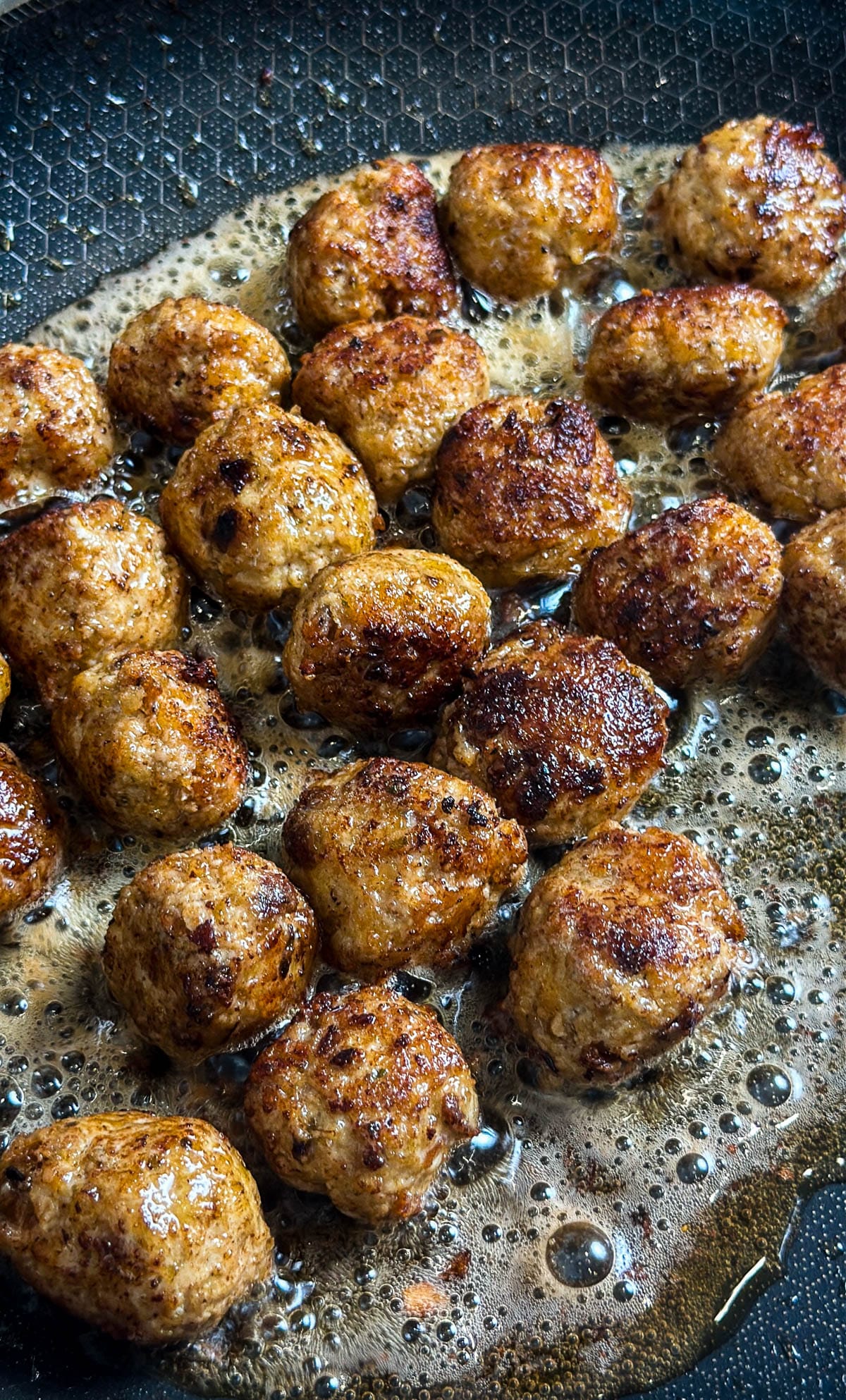 Ground turkey meatballs cooking in oil.