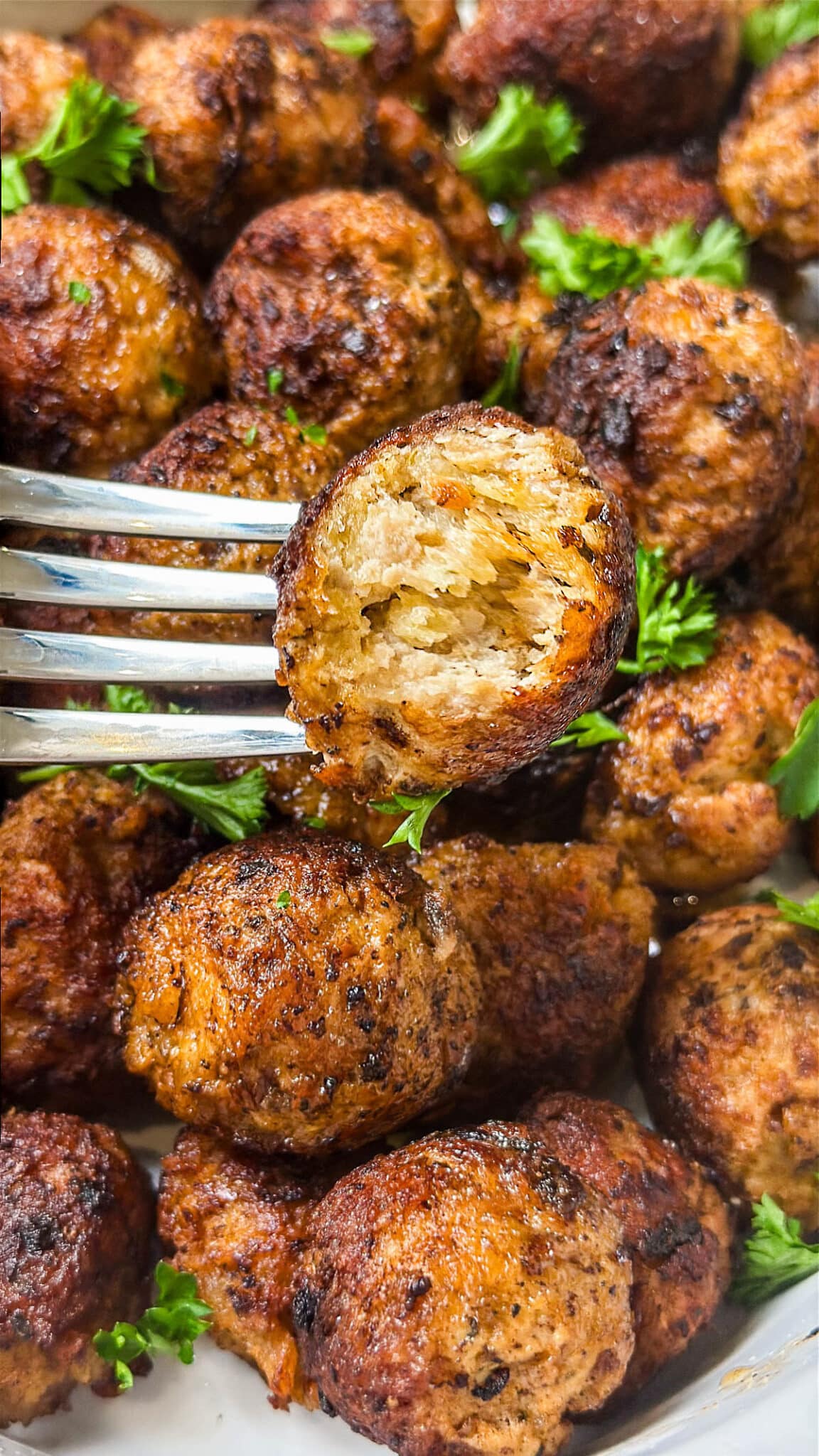 A close-up photo of ground turkey meatballs with one on a fork and the juicy interior showing.