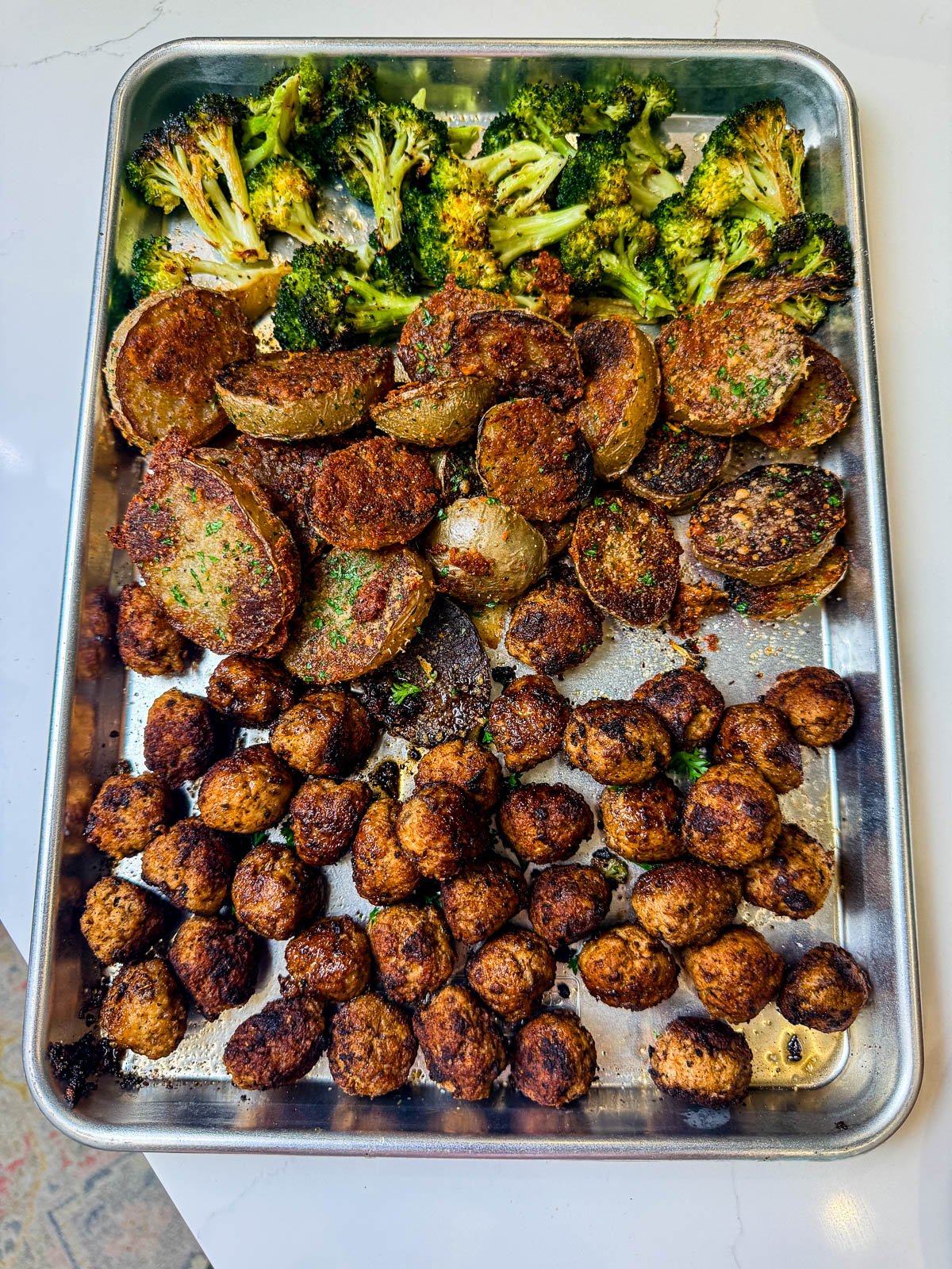 A sheet pan with the ground turkey meatballs, roasted potatoes, and broccoli.