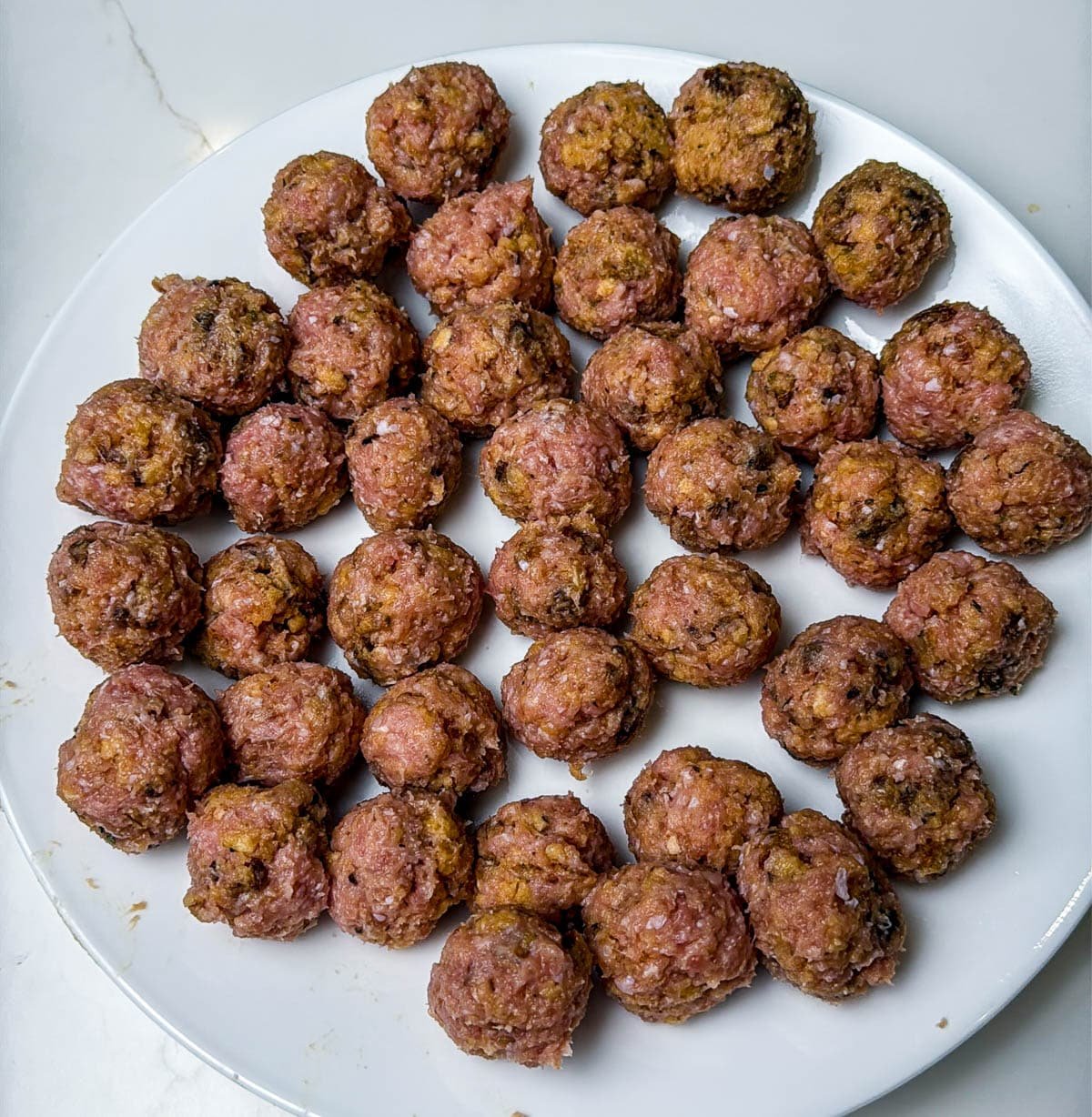 Raw ground turkey meatballs, frozen, and on a plate ready to cook.