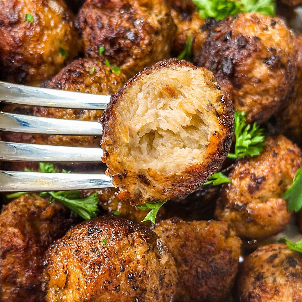 A close-up photo of ground turkey meatballs with one on a fork and the juicy interior showing.