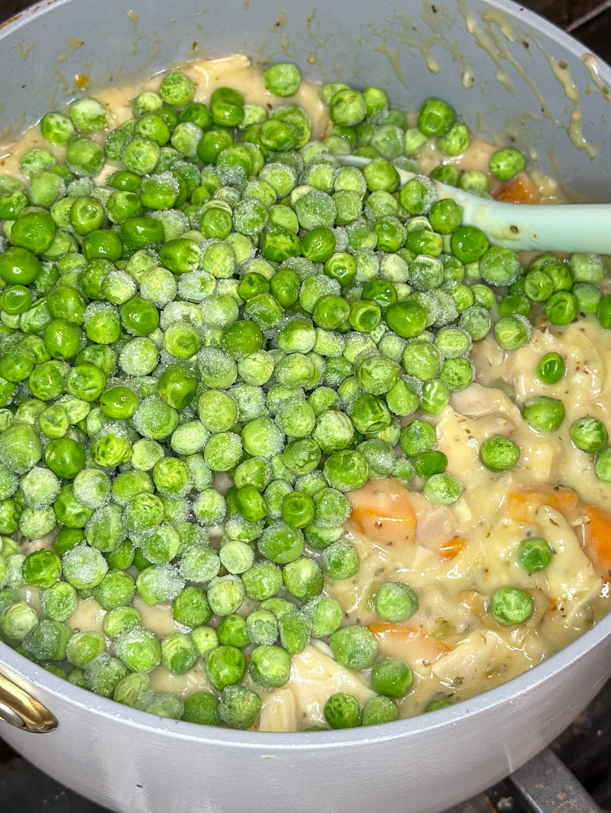 Frozen peas added to the casserole mixture in the saucepan.