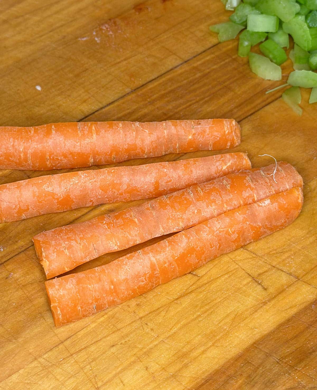 Raw whole carrots cut into fourths on a wooden cutting board.