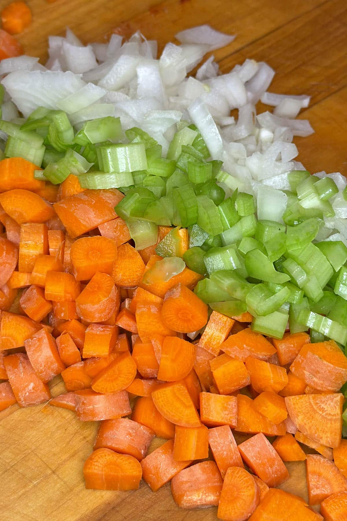 Chopped carrots, celery, and onion on a wooden cutting board.