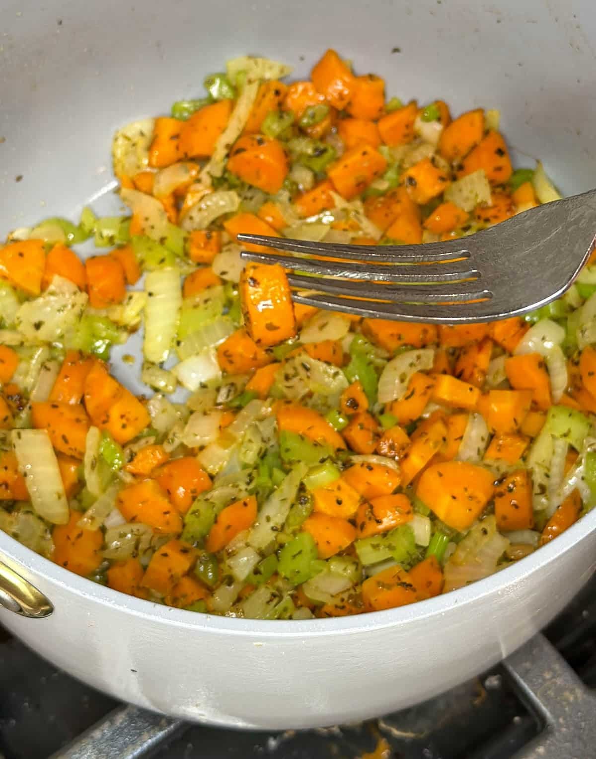 Chopped carrots, celery, and onion cooked to al dente, shown on a fork.