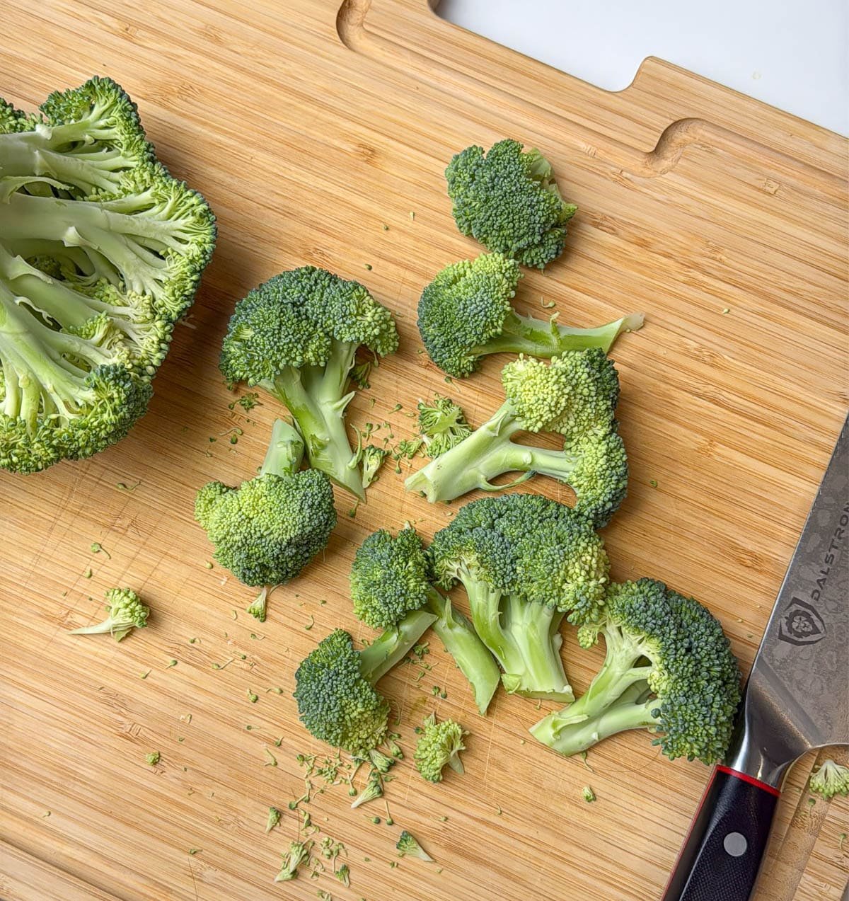Broccoli chopped into small pieces on a wooden cutting board.