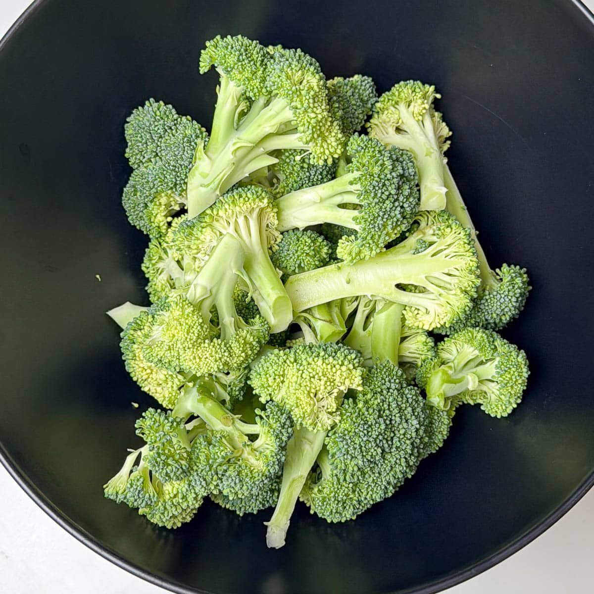 Raw broccoli florets in a black bowl.
