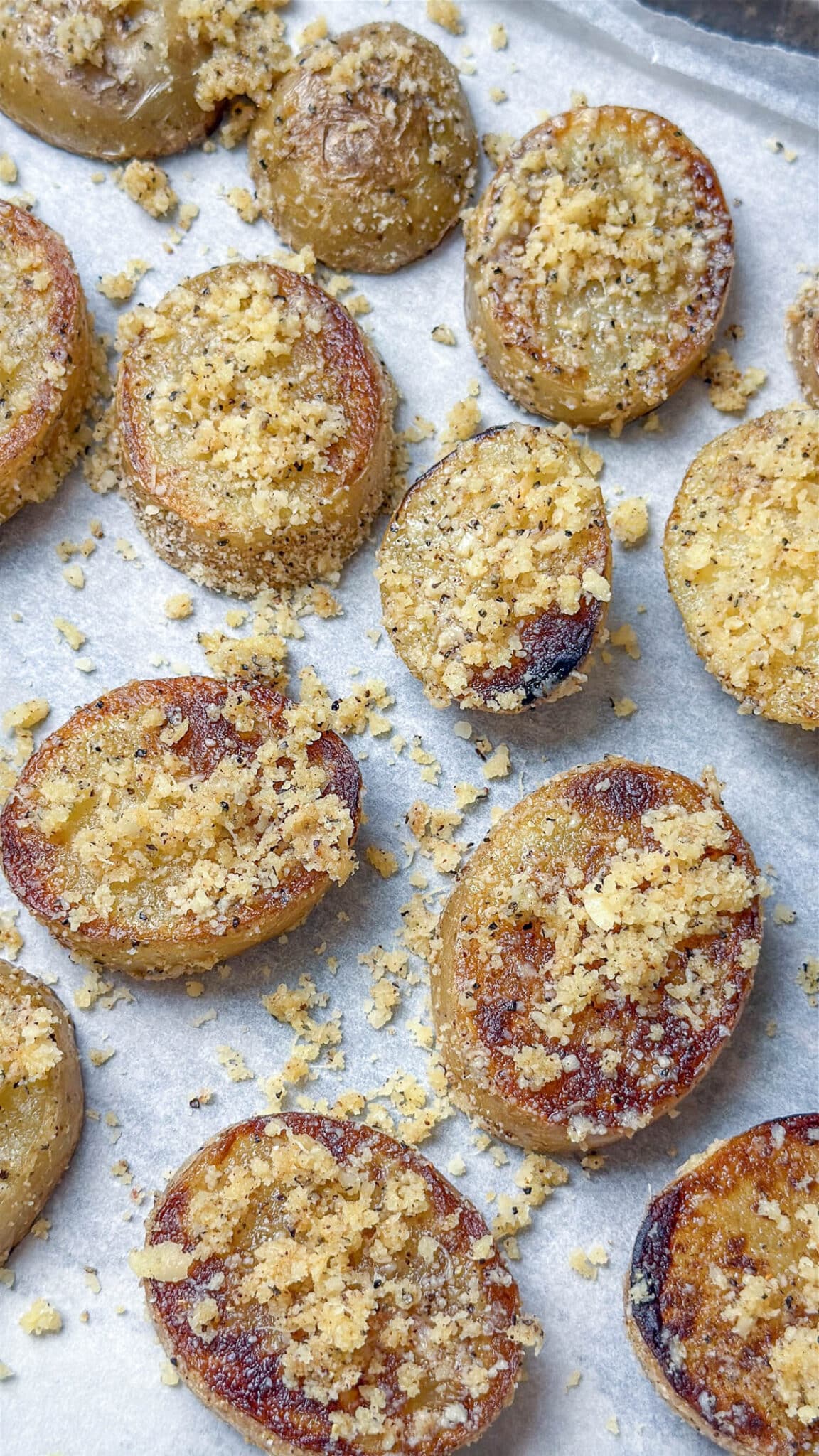 Potato slices placed on a baking sheet with more of the parmesan cheese mixture on top of each slice.