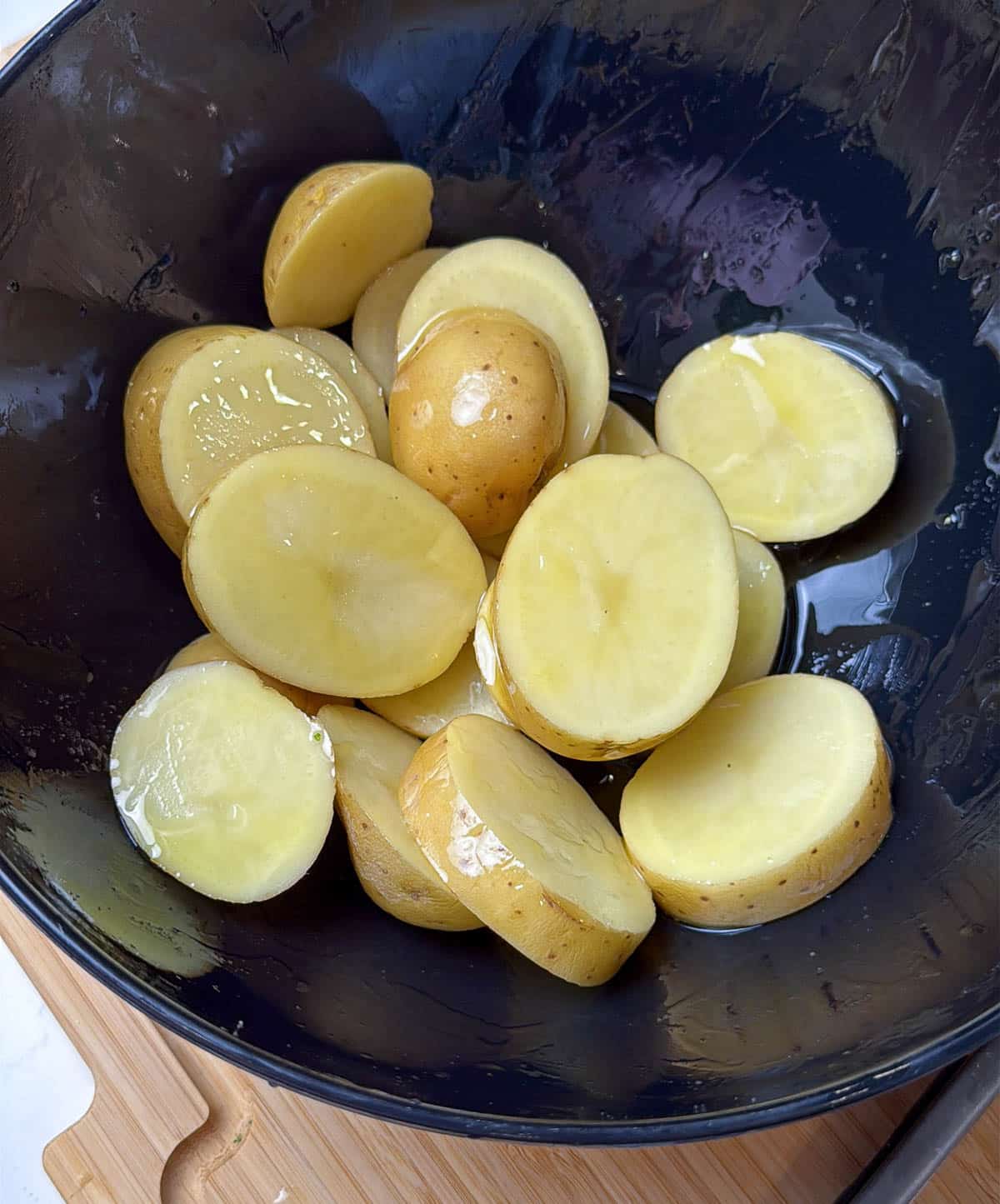 Potato slices coated in olive oil in a large bowl.