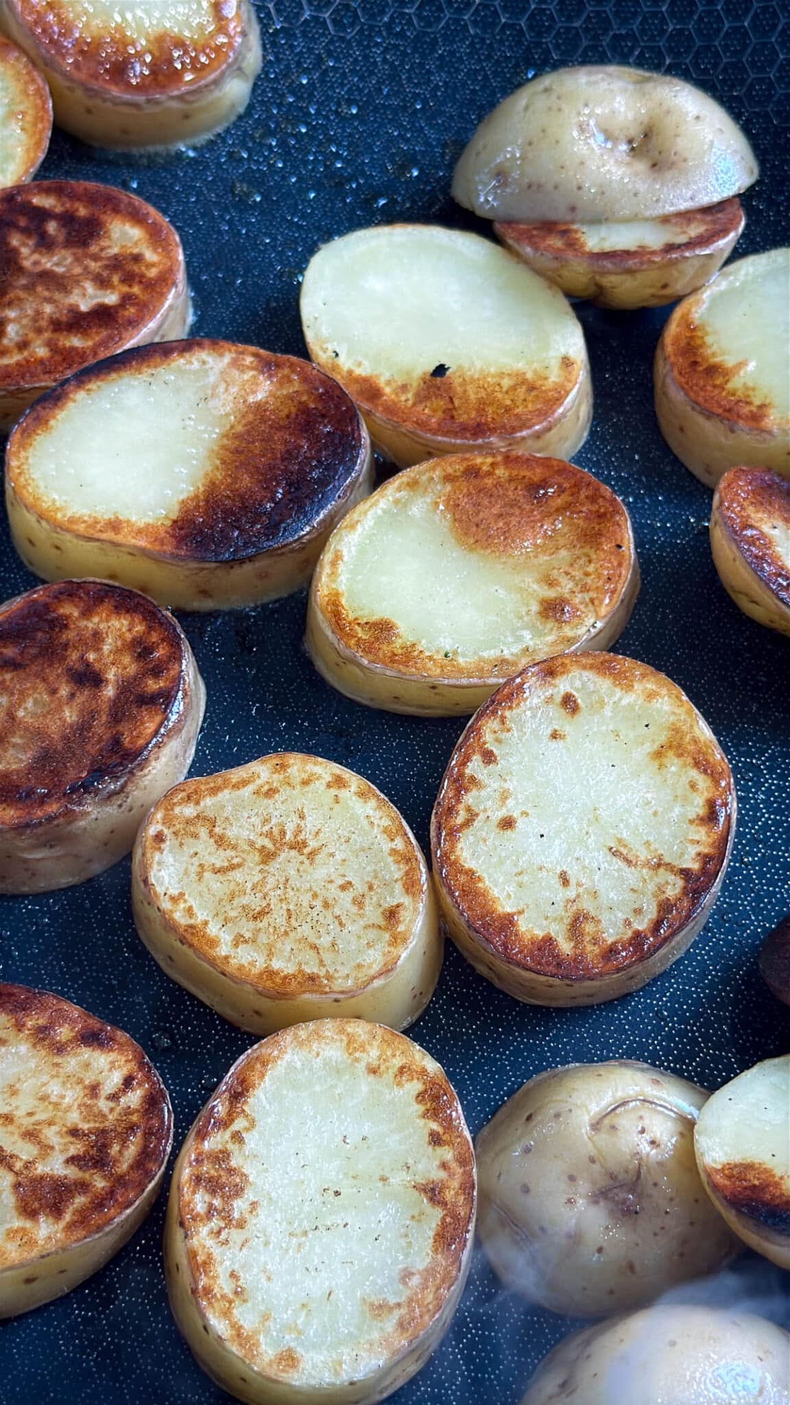 Browned potato slices cooking in a skillet.