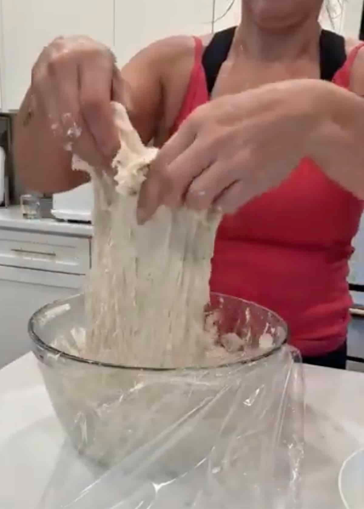 Hands stretching sourdough douh up out of a glass bowl.