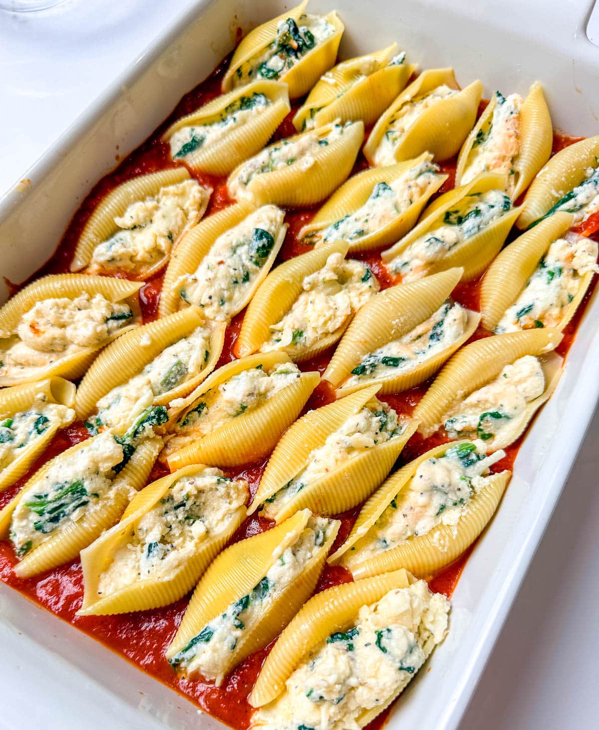Stuffed pasta shells lined up and placed in the marinara sauce coated baking dish.