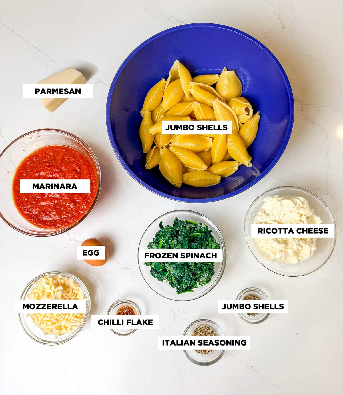 Ingredient shot for Stuffed Shells, featuring: jumbo shells, marinara sauce, ricotta cheese, mozzarella, parmesan cheese, frozen spinach, an egg, chili flakes, Italian seasoning, and SGP.