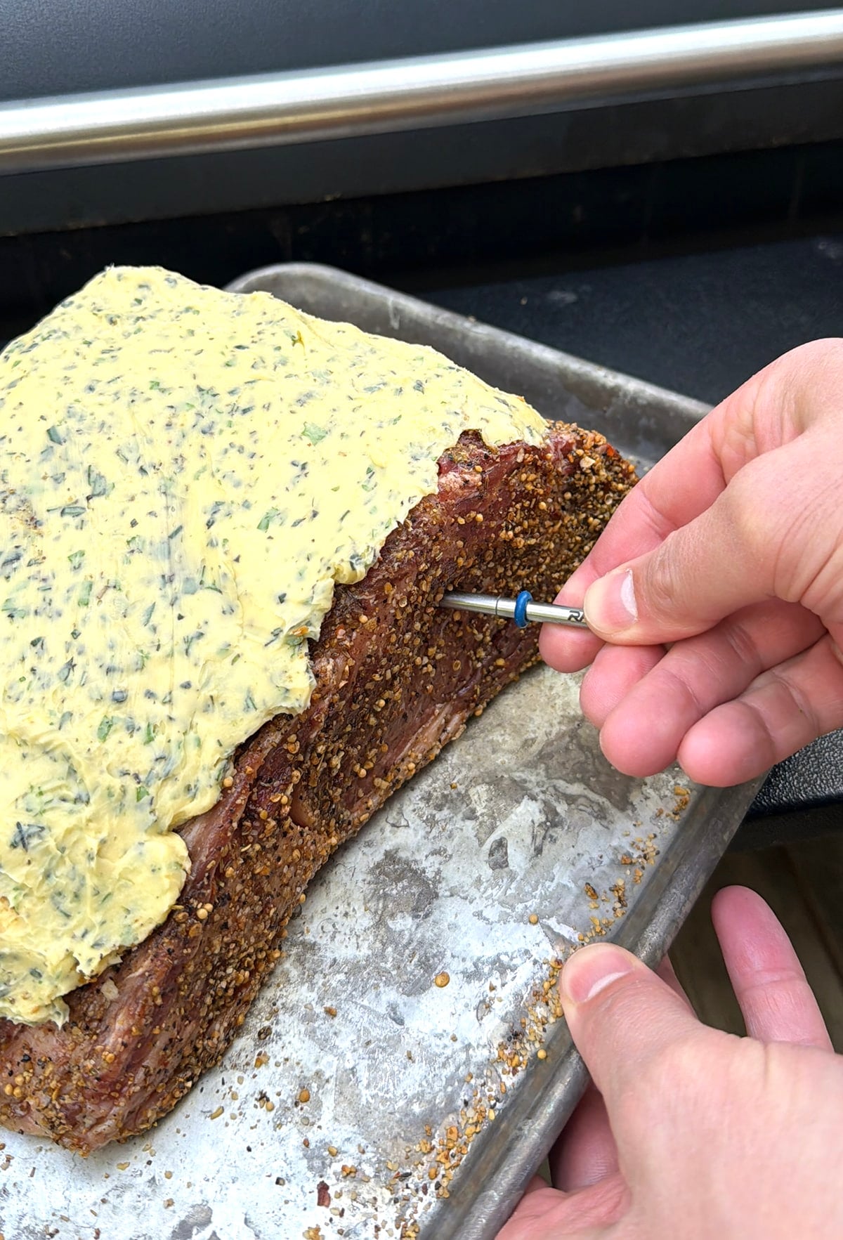 Hand inserting a metal probe into a prepared prime rib roast.