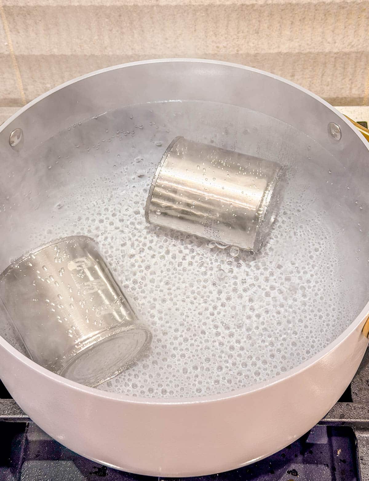 two cans of sweetened condensed milk in a pot of simmering water