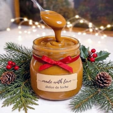 spooning a jar of dulce de leche surrounded by christmas greenery