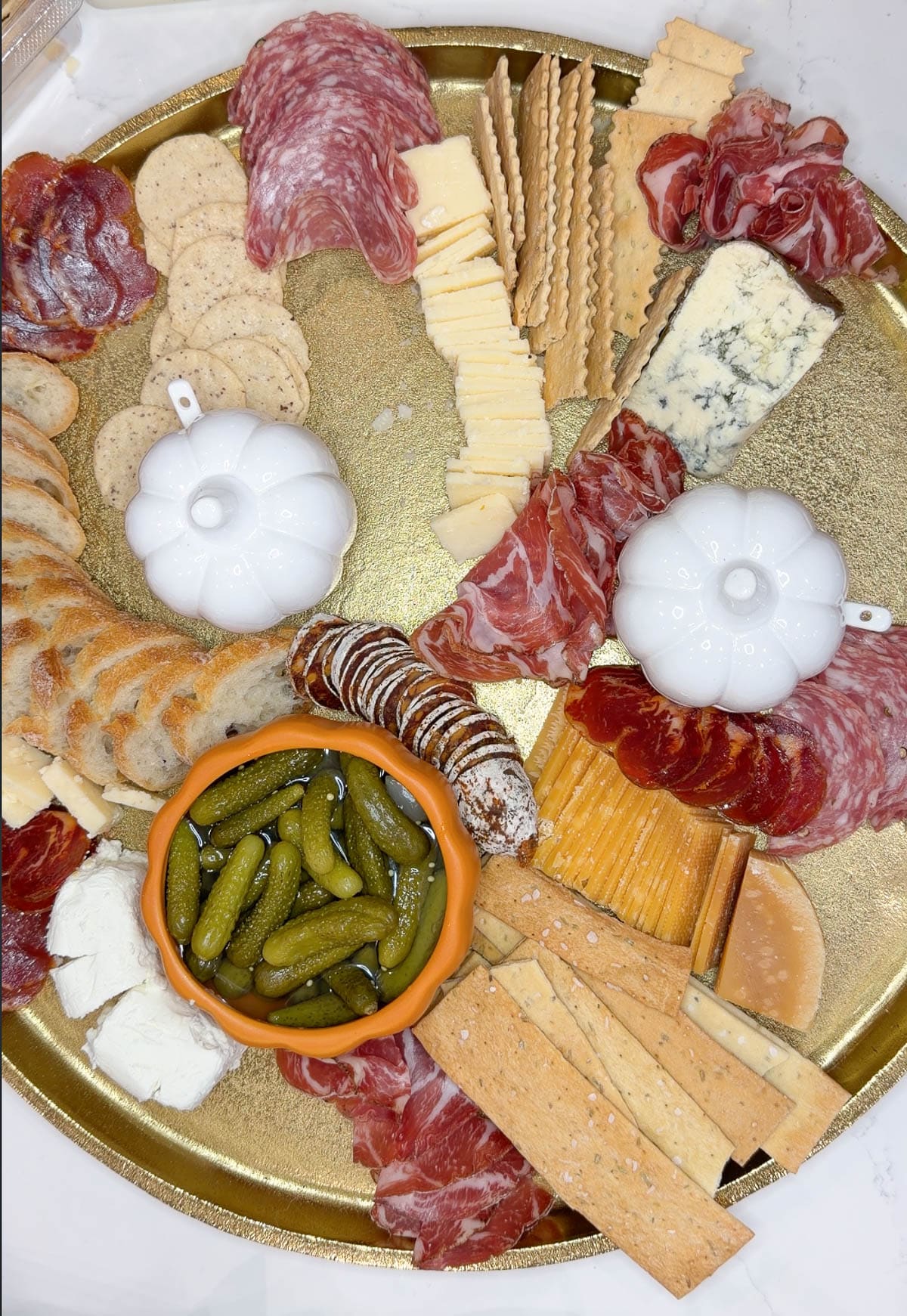 A gold tray with cut cheeses, bread, crackers, meats, and pickles on it.
