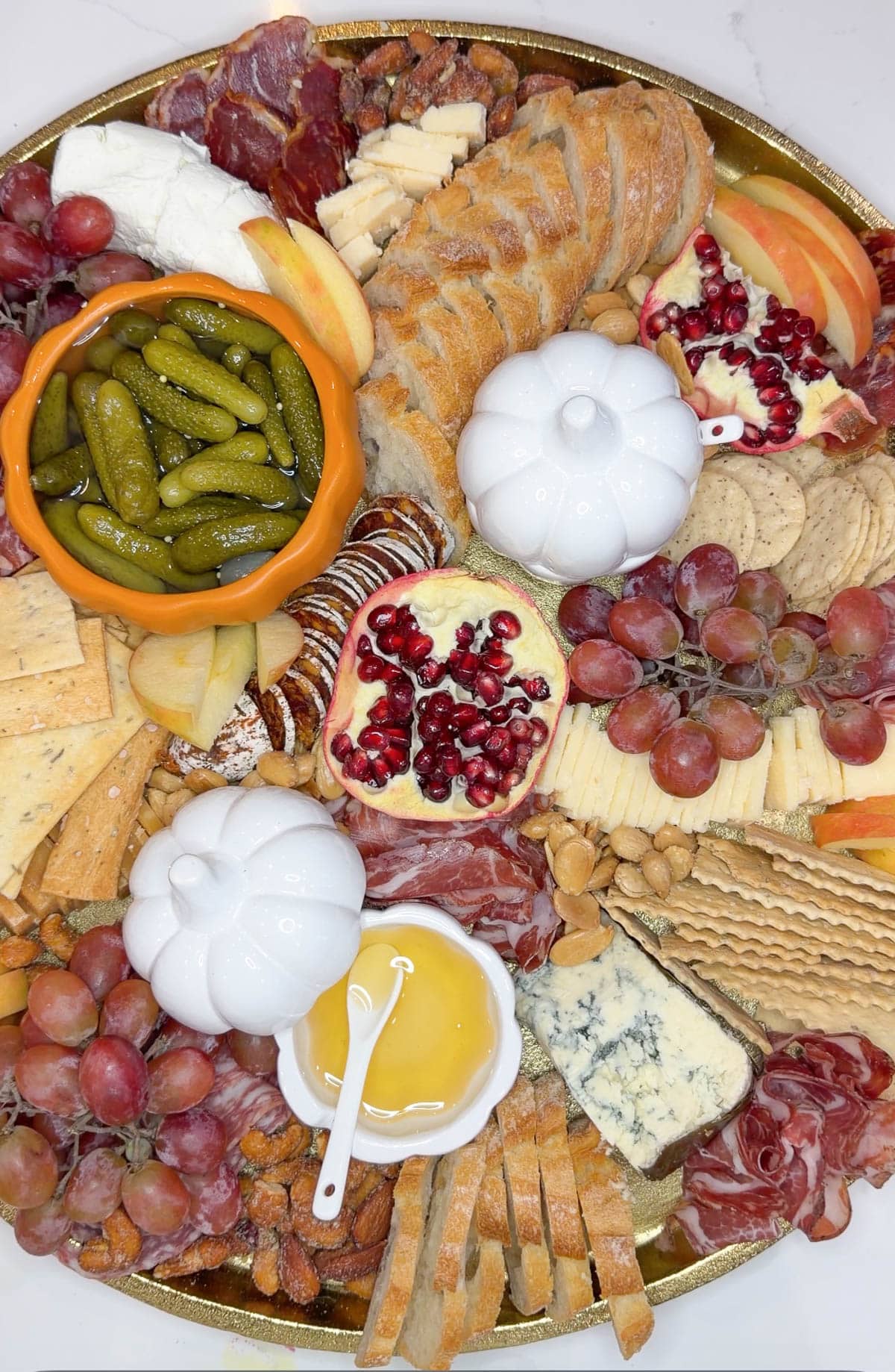 A gold tray with cut cheeses, bread, crackers, meats, fruits, and pickles on it.