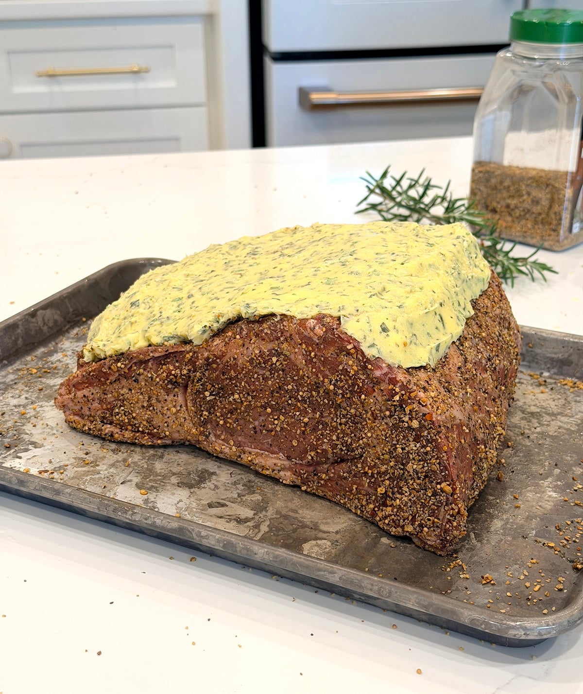 Prime rib roast covered in rub and compound butter on a metal pan.