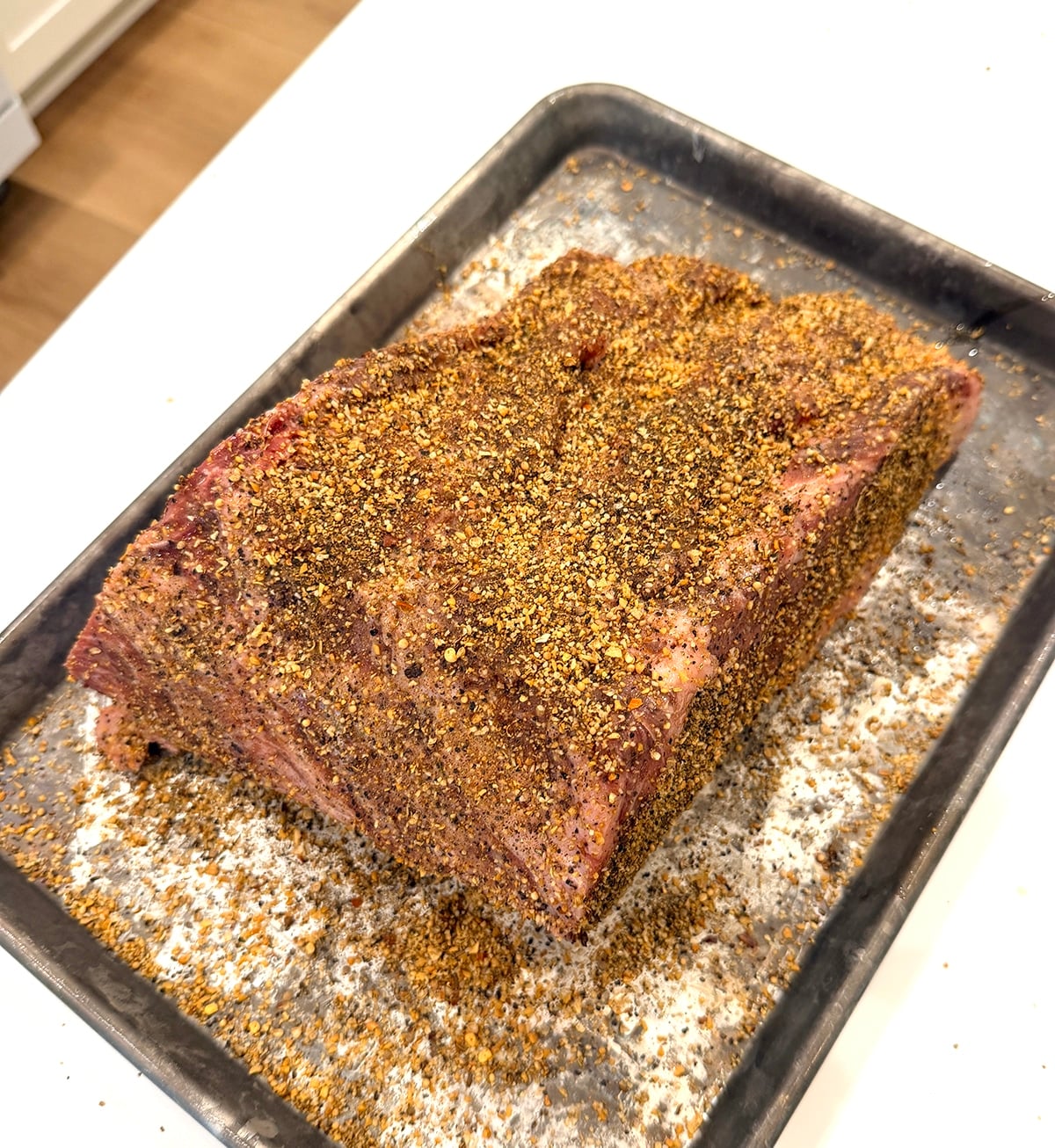 Prime rib coated in rub on a metal pan.