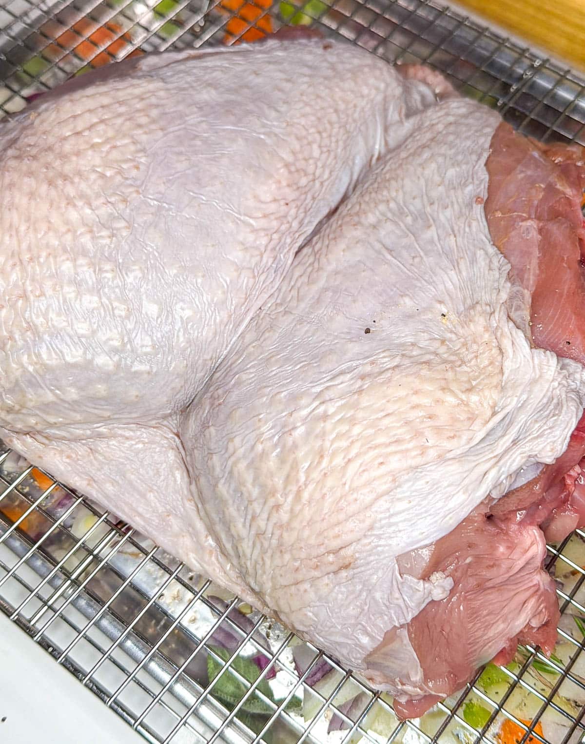 The turkey breast on a baking rack over the vegetables and herbs on a baking sheet.