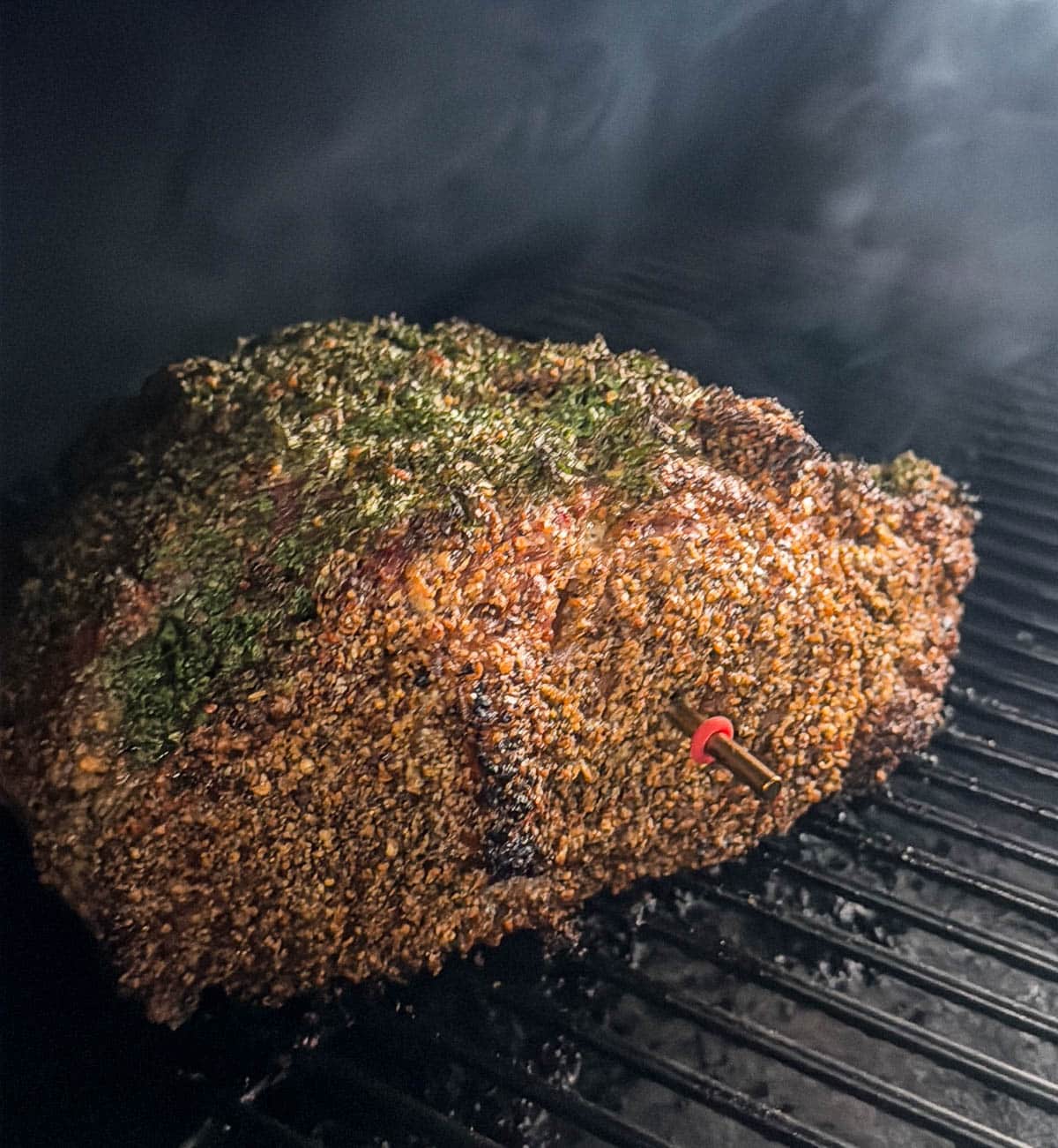 A whole, seasoned and cooked prime rib in the smoker with a probe thermometer in the middle.