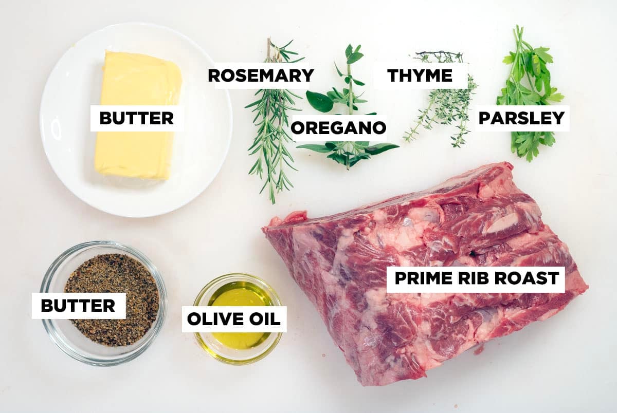 Ingredient shot for Smoked Prime Rib, featuring: butter, fresh herbs, seasoning, olive oil, and a raw prime rib roast.