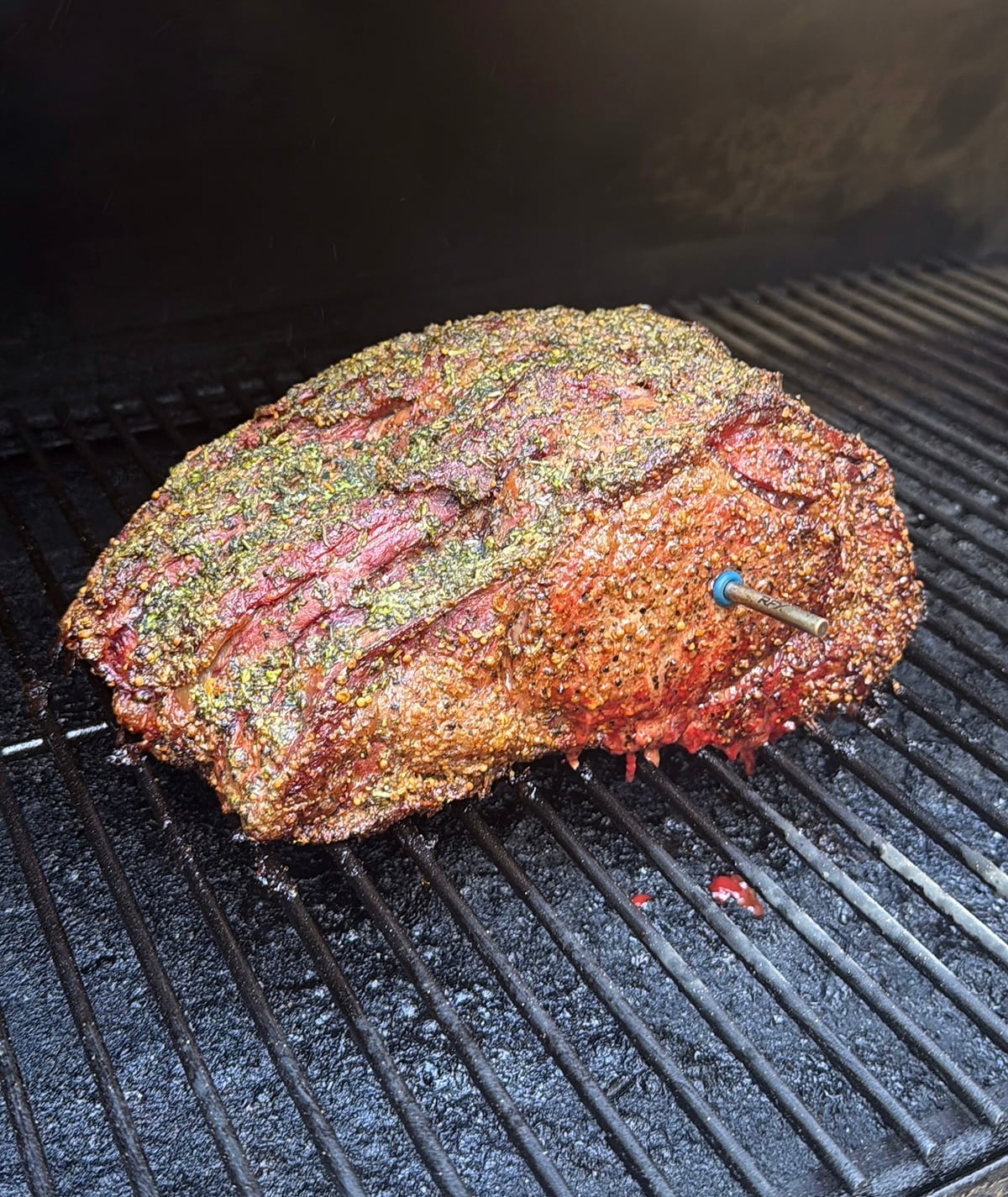 Close up of finished smoked prime rib roast with a probe thermometer on a grill.