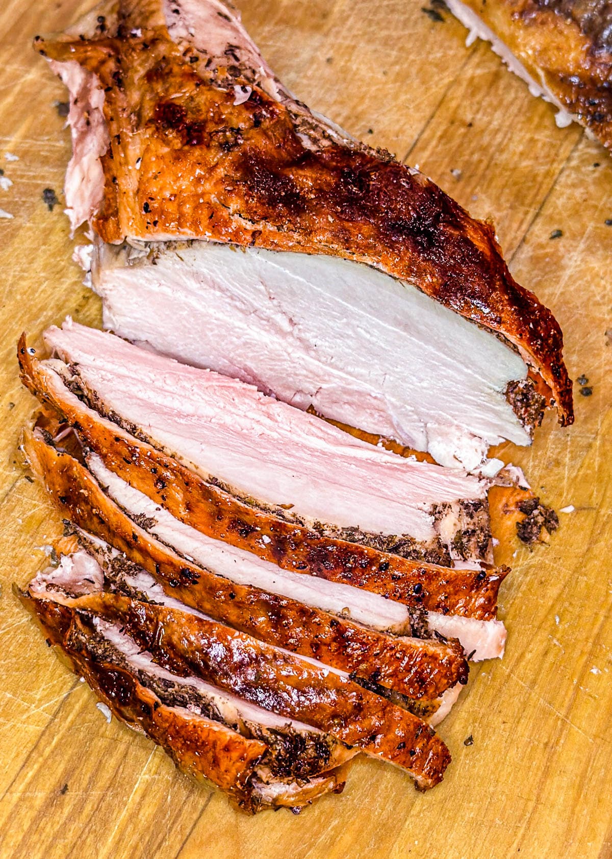 A close-up photo of a sliced spatchcocked turkey breast on a wooden cutting board.