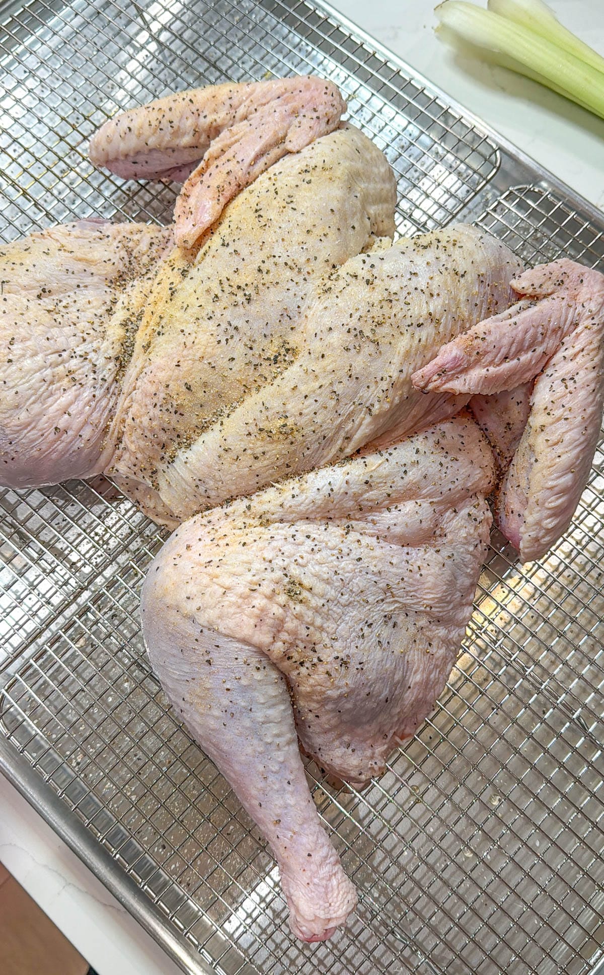 A raw, seasoned spatchcock turkey on a wire rack.