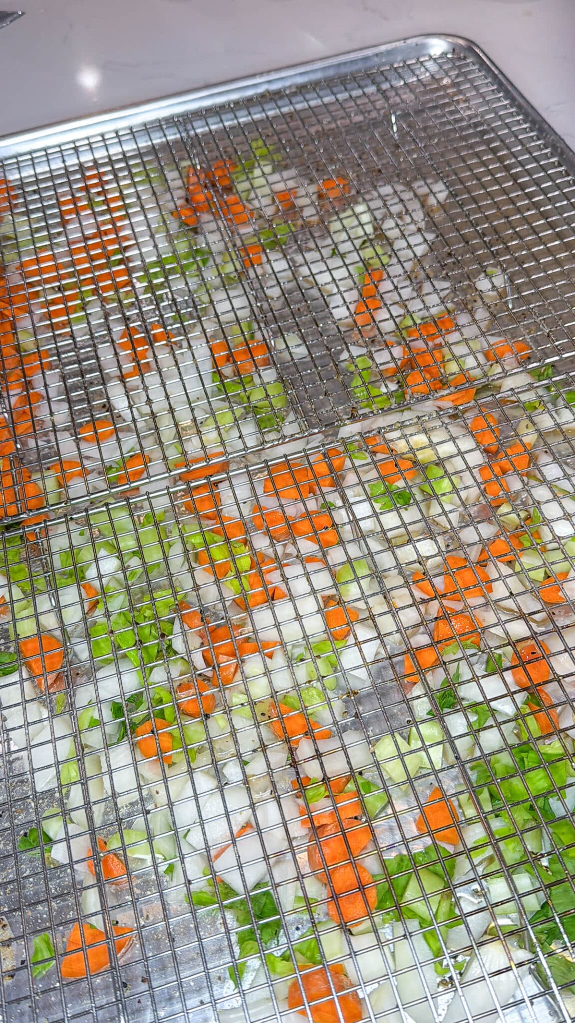 Chopped onion, carrots, and celery spread evenly on a baking sheet with a wire rack on top.