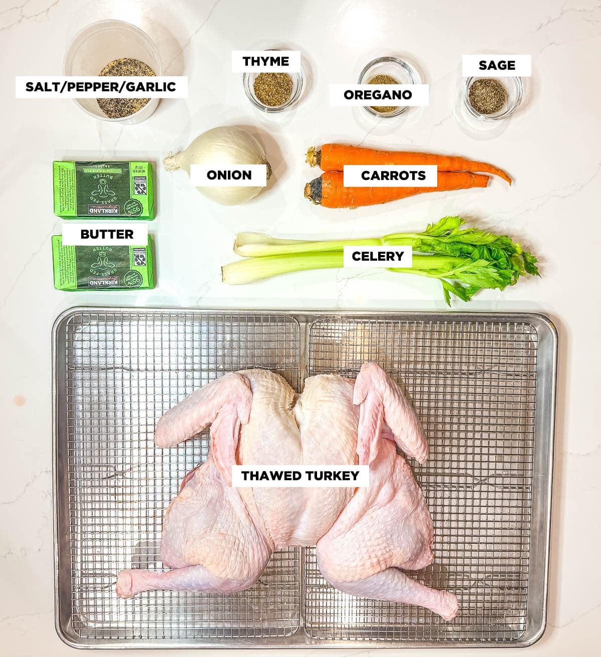 Ingredient shot for spatchcock turkey, featuring: salt, pepper, garlic powder, thyme, oregano, sage, onion, carrots, celery, butter, and a whole, thawed turkey.