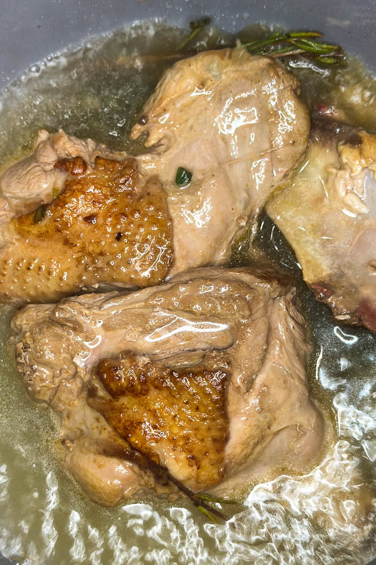 Turkey bones and giblets in a pot with fresh herbs on top and added water.