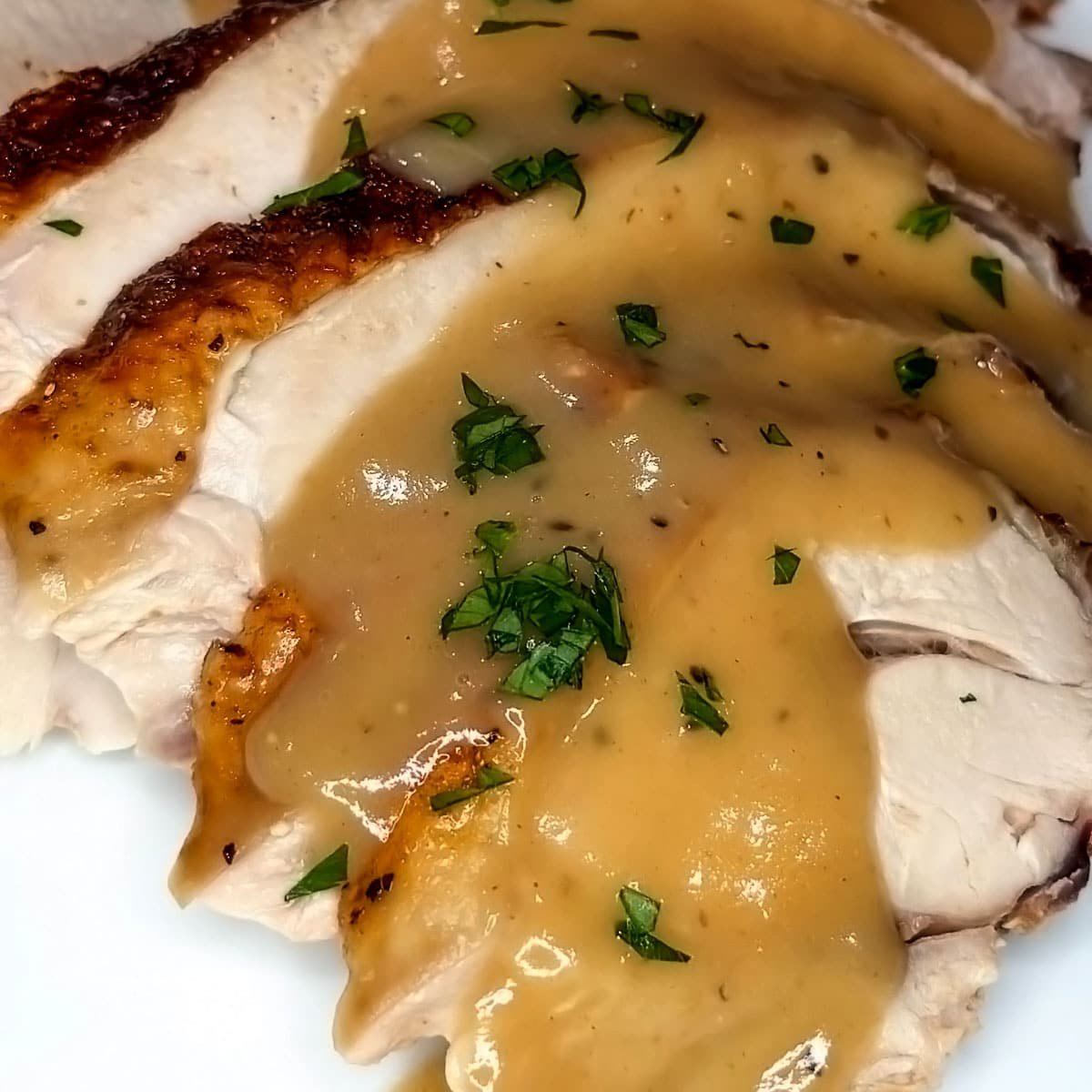 Close-up photo of turkey gravy on slices of turkey breast.