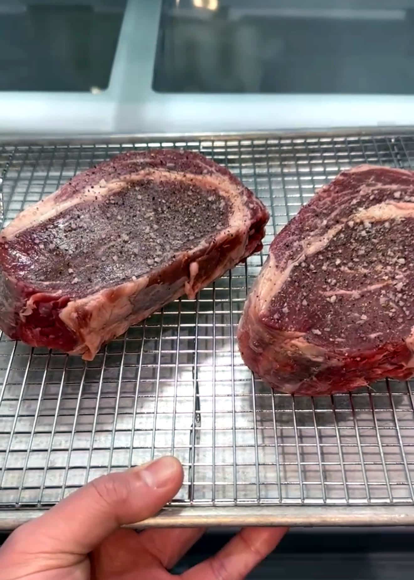 two ribeye steaks dry brining on a metal rack