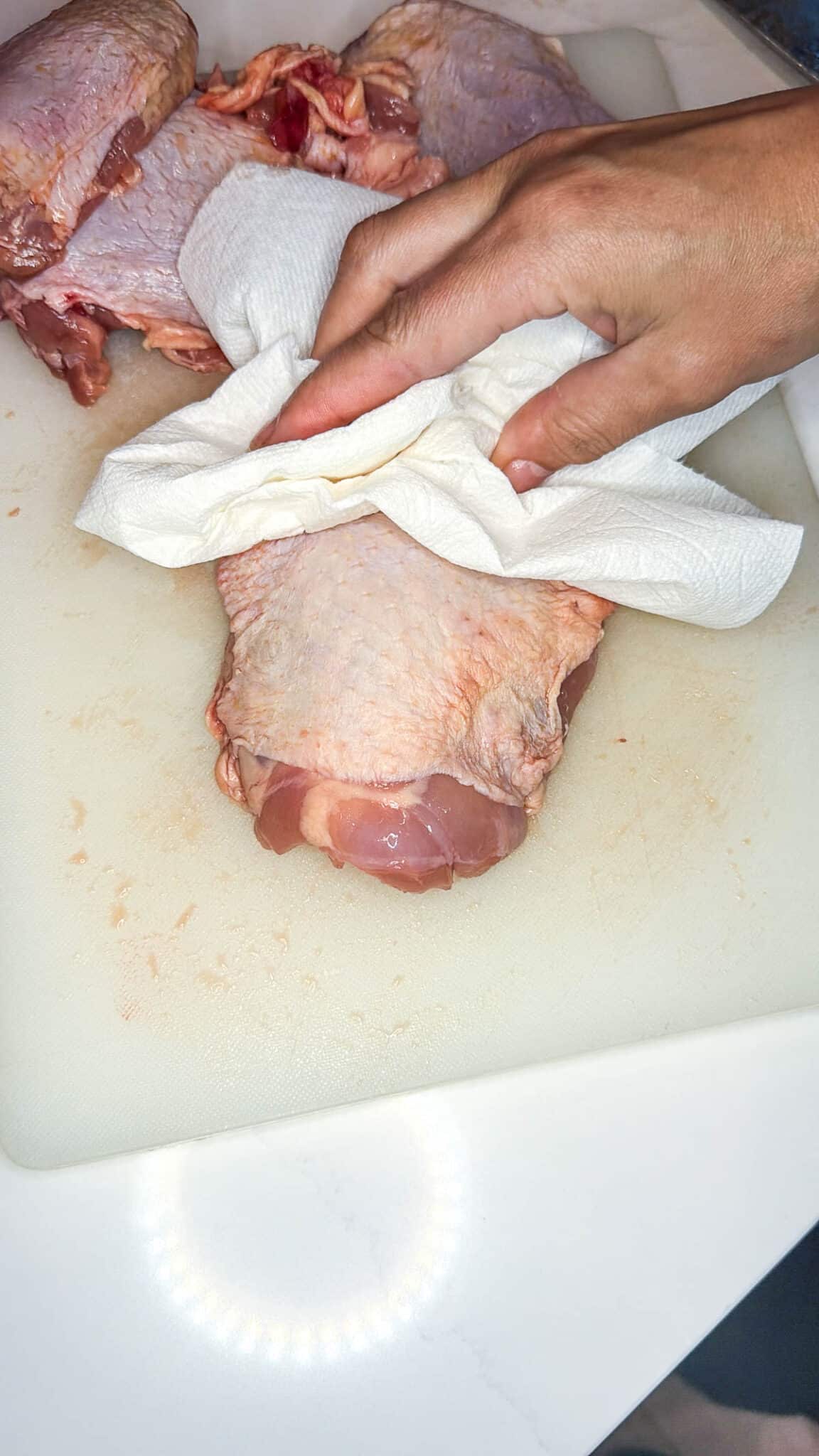 Hand drying raw chicken thigh with a paper towel.
