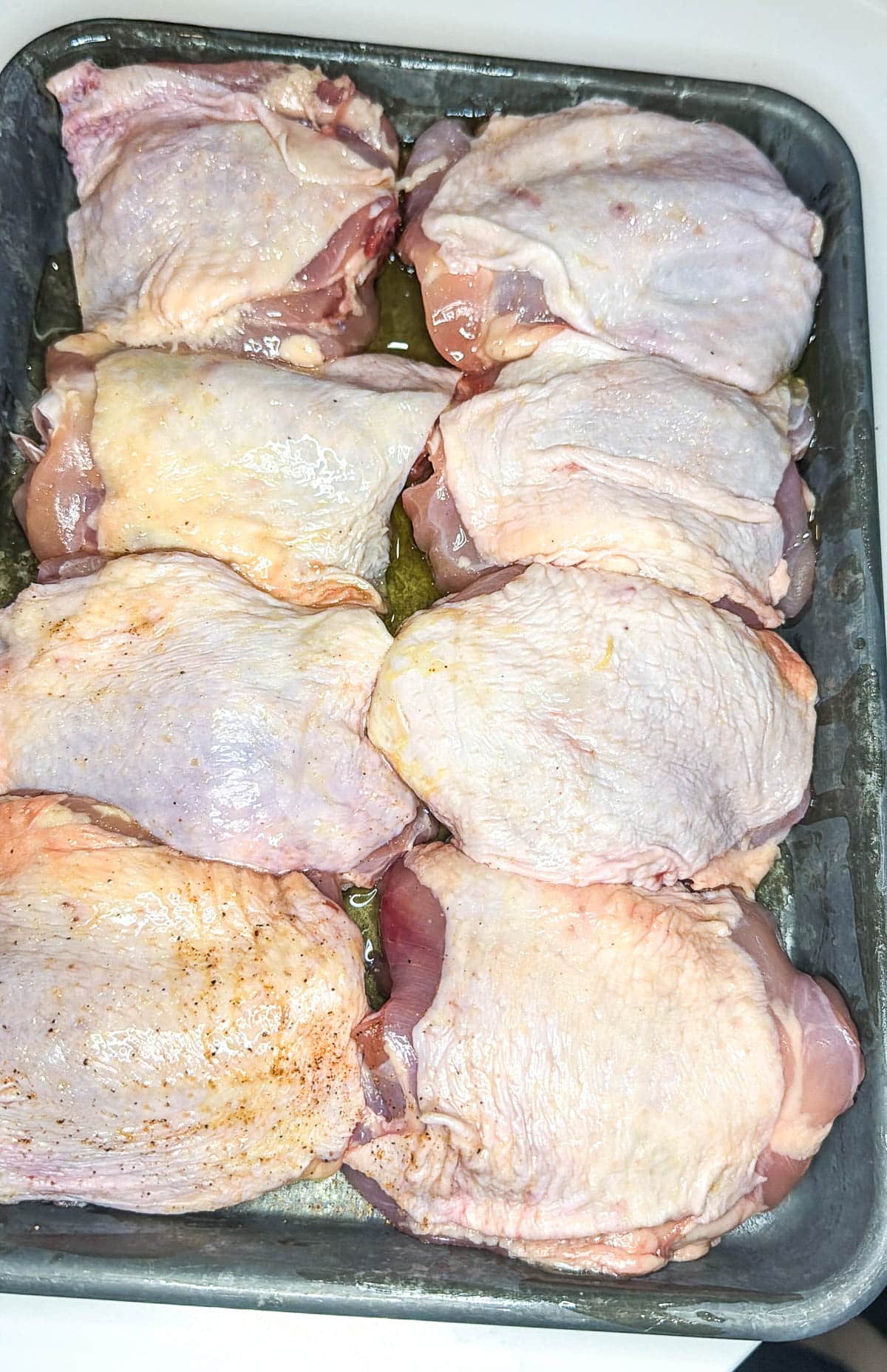 Eight chicken thighs coated in oil on a metal sheet pan.