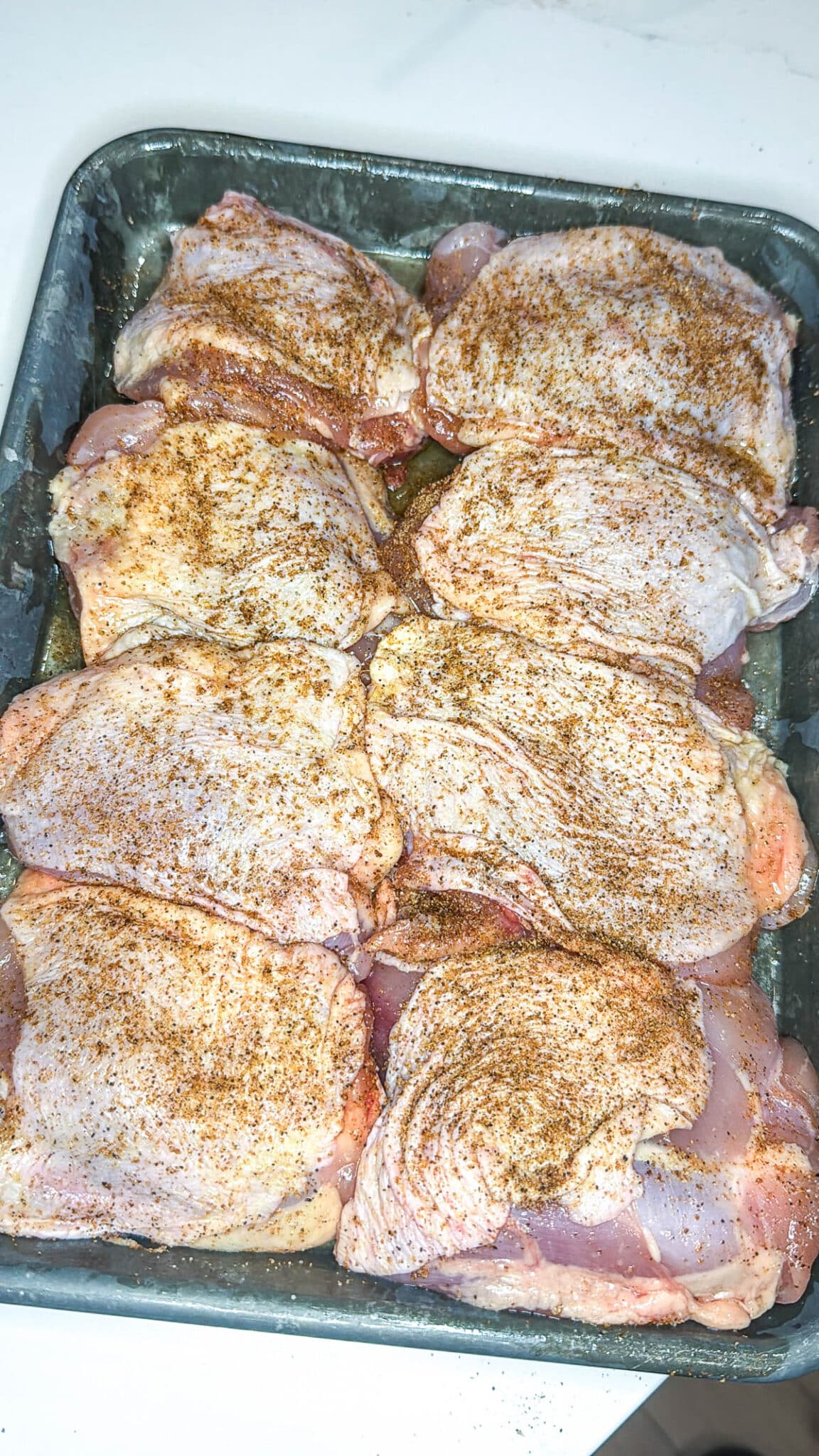 Seasoned chicken thighs on a metal sheet pan.