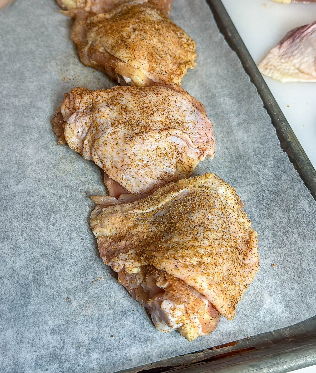 Three chicken thighs on a metal sheet pan coated with seasoning.