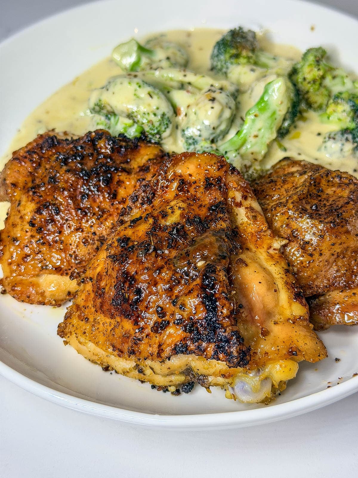 Three crispy chicken thighs on a plate with broccoli in the background on a plate.