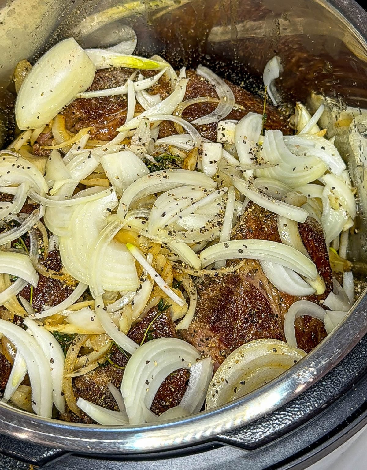 Seared chuck roast and onion mixture in an instant pot.