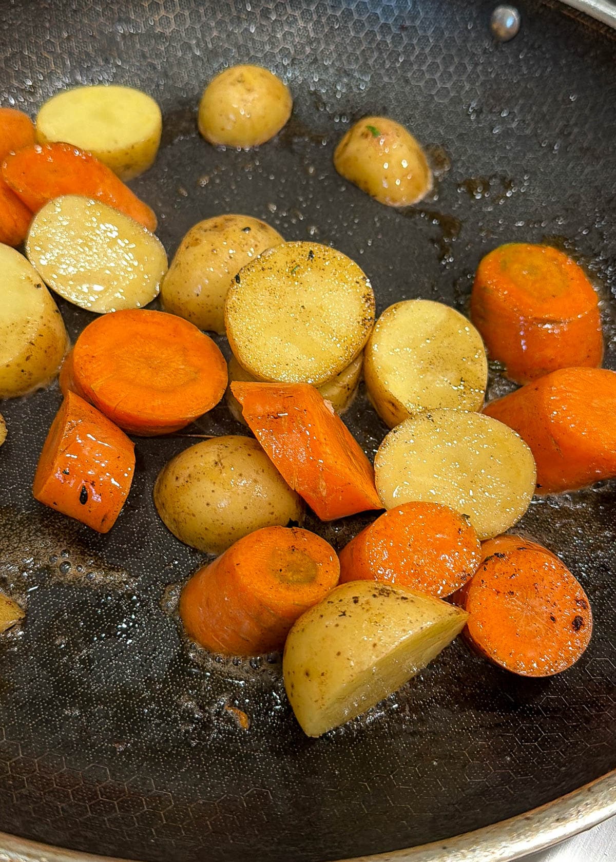 Carrots and potatoes searing in a black pan.