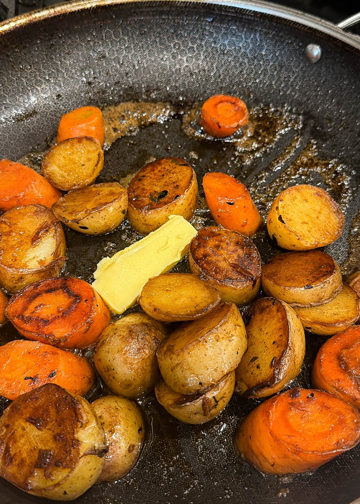 Browned potatoes and carrots in a pan with butter and pan drippings.