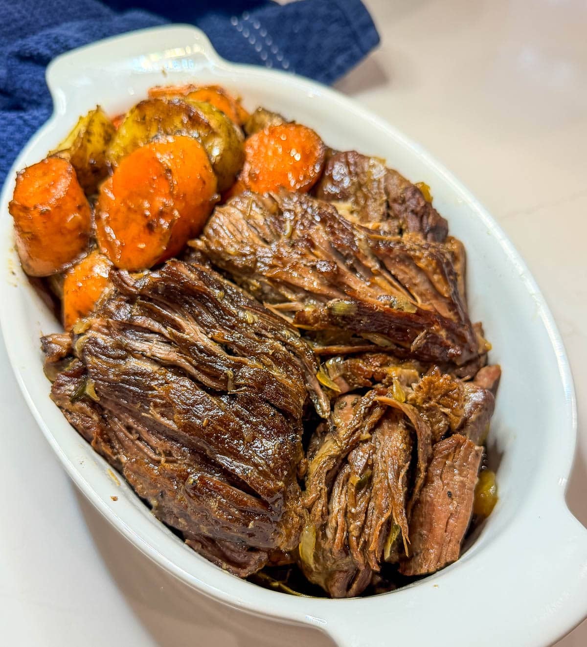 Tender beef in a white dish with carrots and potatoes.