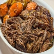 Tender pot roast in a white dish with potatoes and carrots.