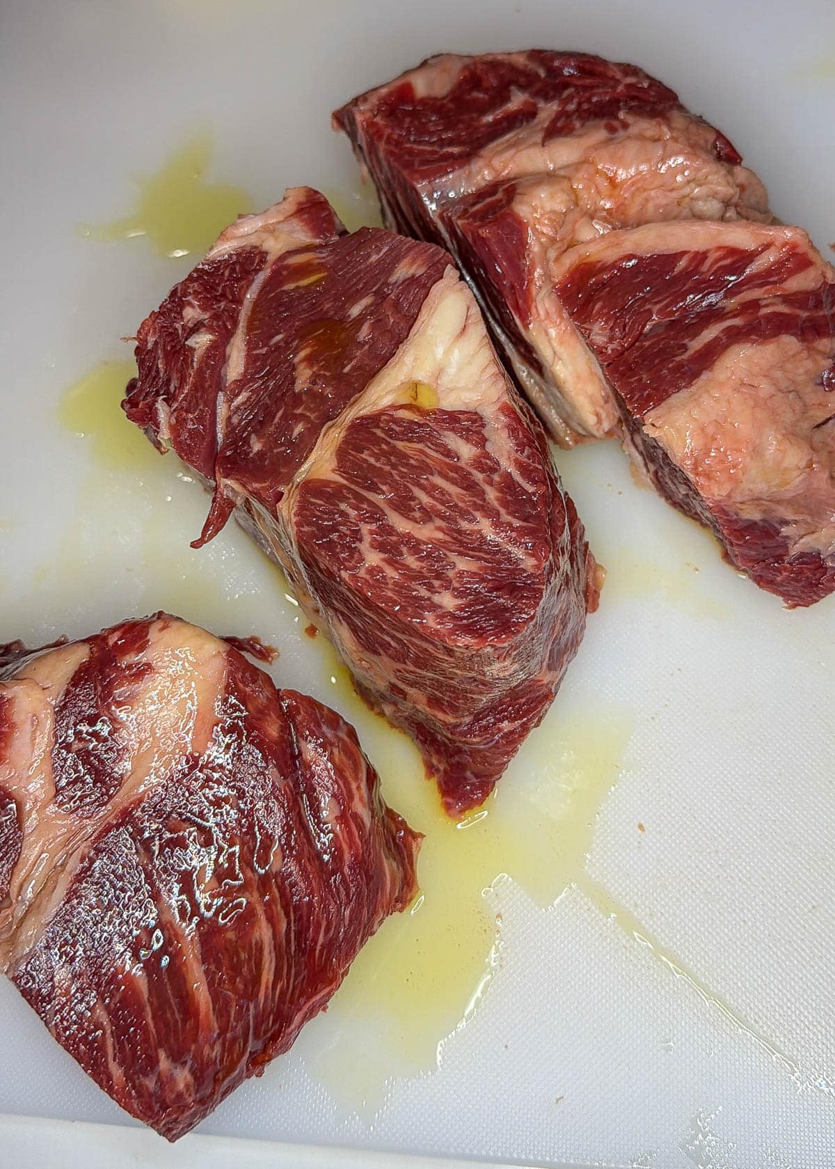 Pot roast cut into three sections coated in olive oil on a white cutting board.