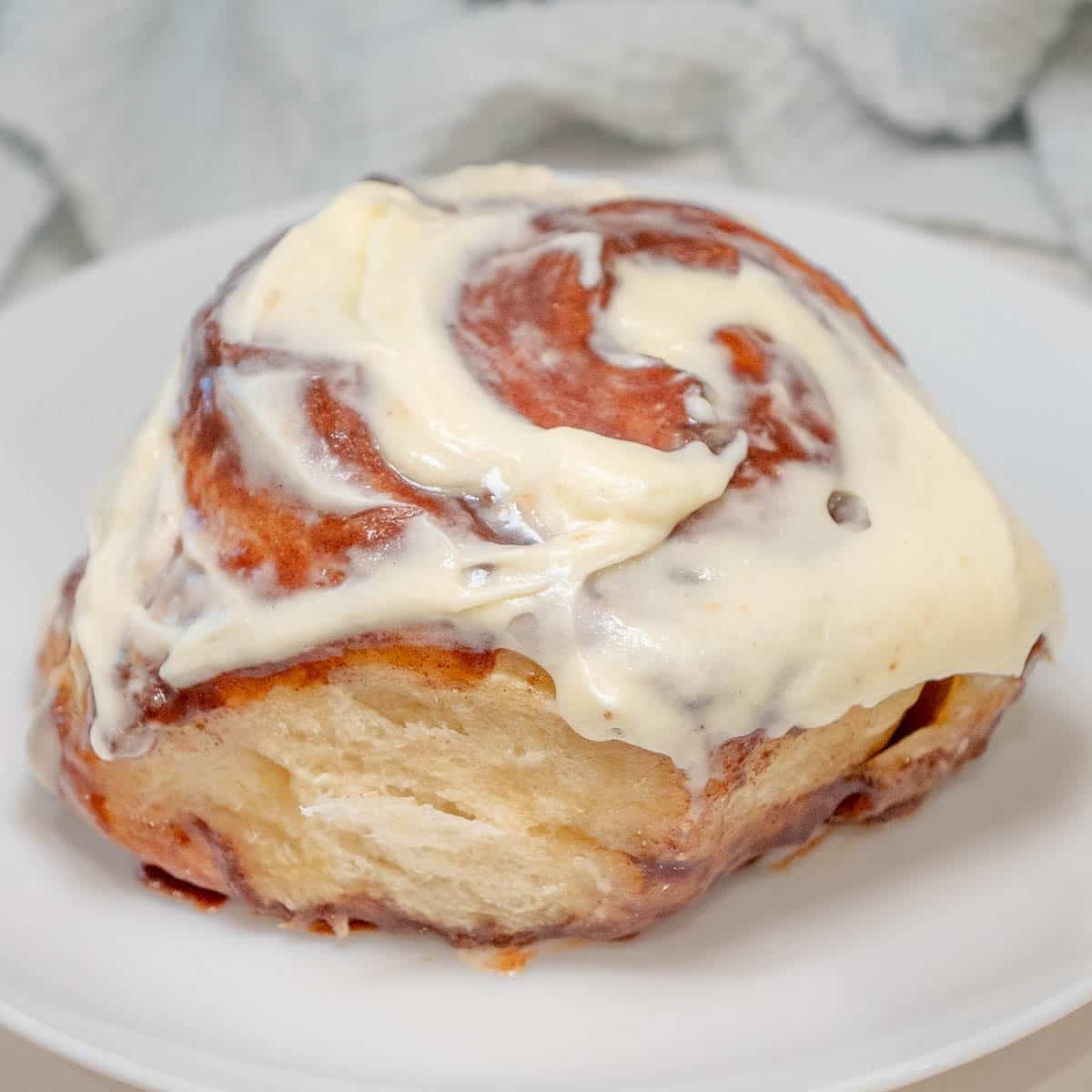 Close up of a frosted cinnamon roll on a white plate.